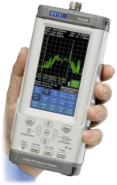 A portable RF spectrum analyser is held in one hand. The display shows a frequency analysis with a prominent signal peak value.