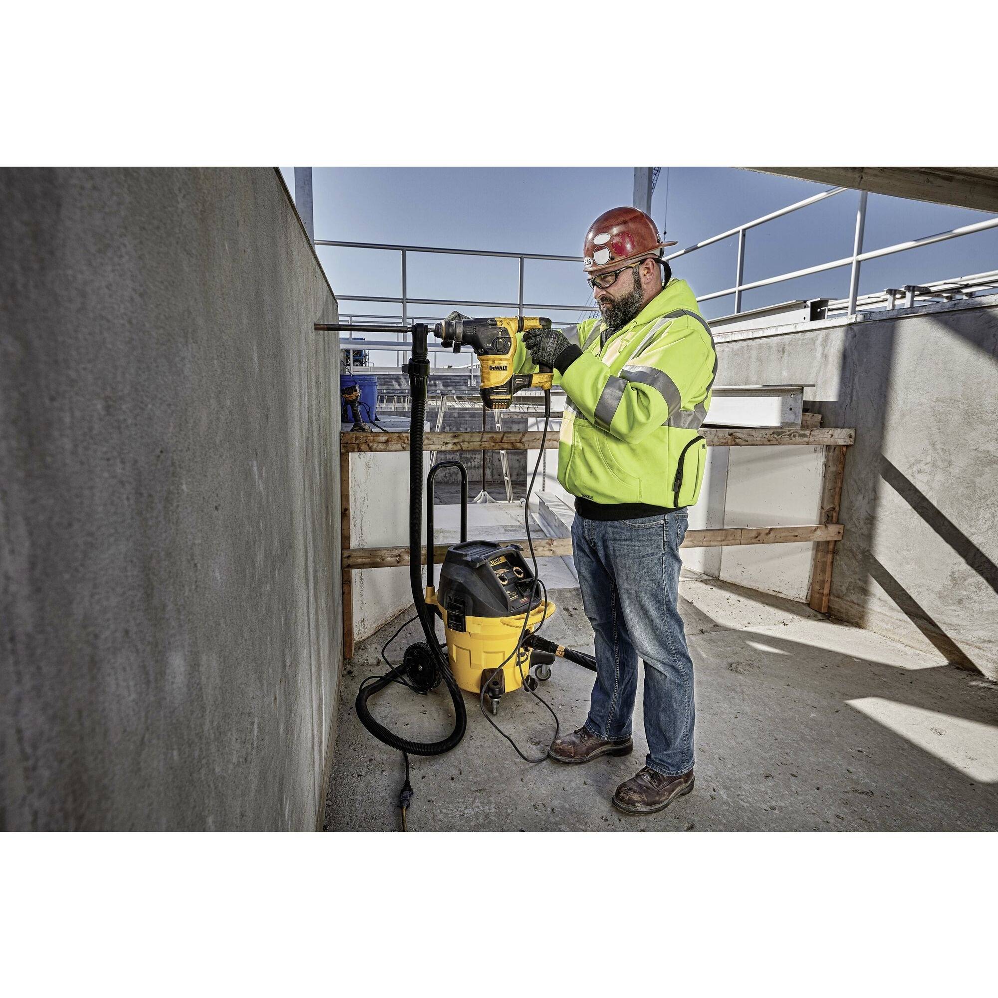 A construction worker in a yellow protective suit and red hard hat is drilling into a concrete wall on a building site.