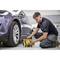 A man in workwear is inflating the tyres of a grey car with a portable air compressor in a garage.