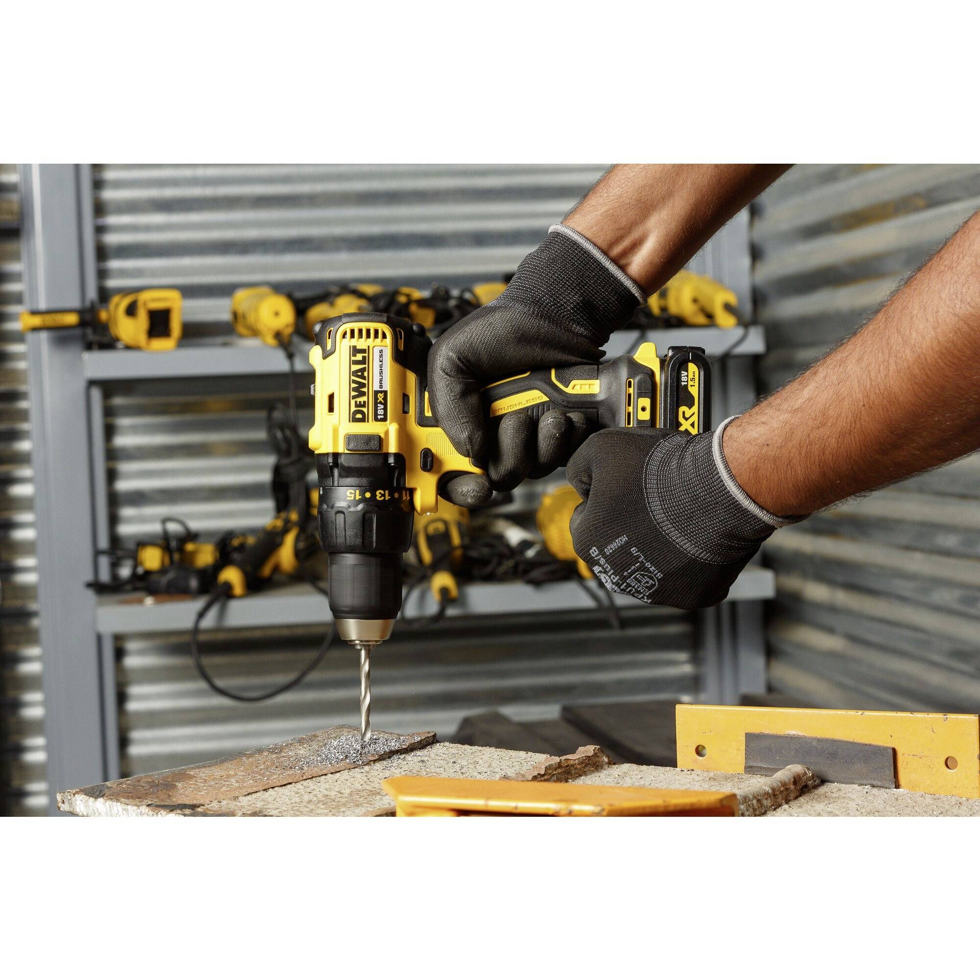 A person is drilling into a piece of wood with a yellow, cordless drill. Other tools can be seen in the background.