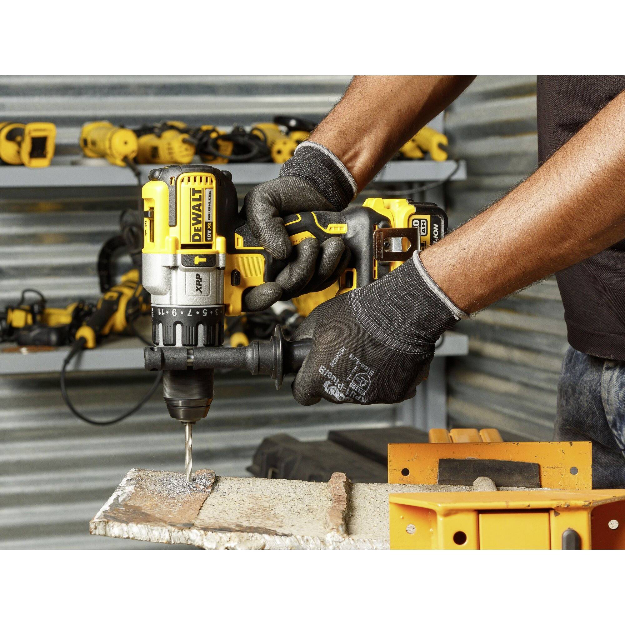A person is working with a yellow cordless drill driver on metal. Additional tools are visible in the background.