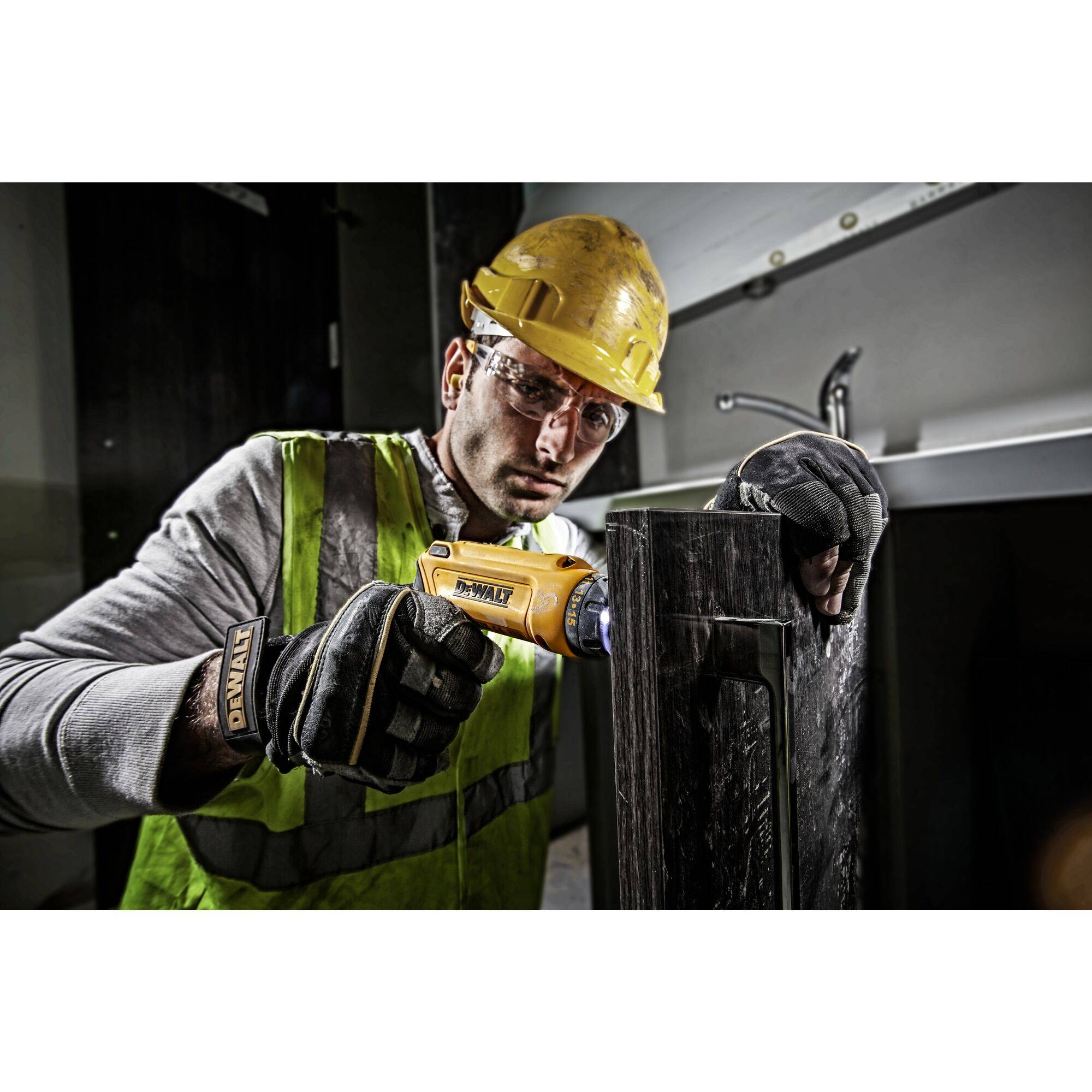 A construction worker wearing a hard hat and hi-vis vest is using electric tools to work with metal, focusing on precise workmanship, in an indoor work environment.