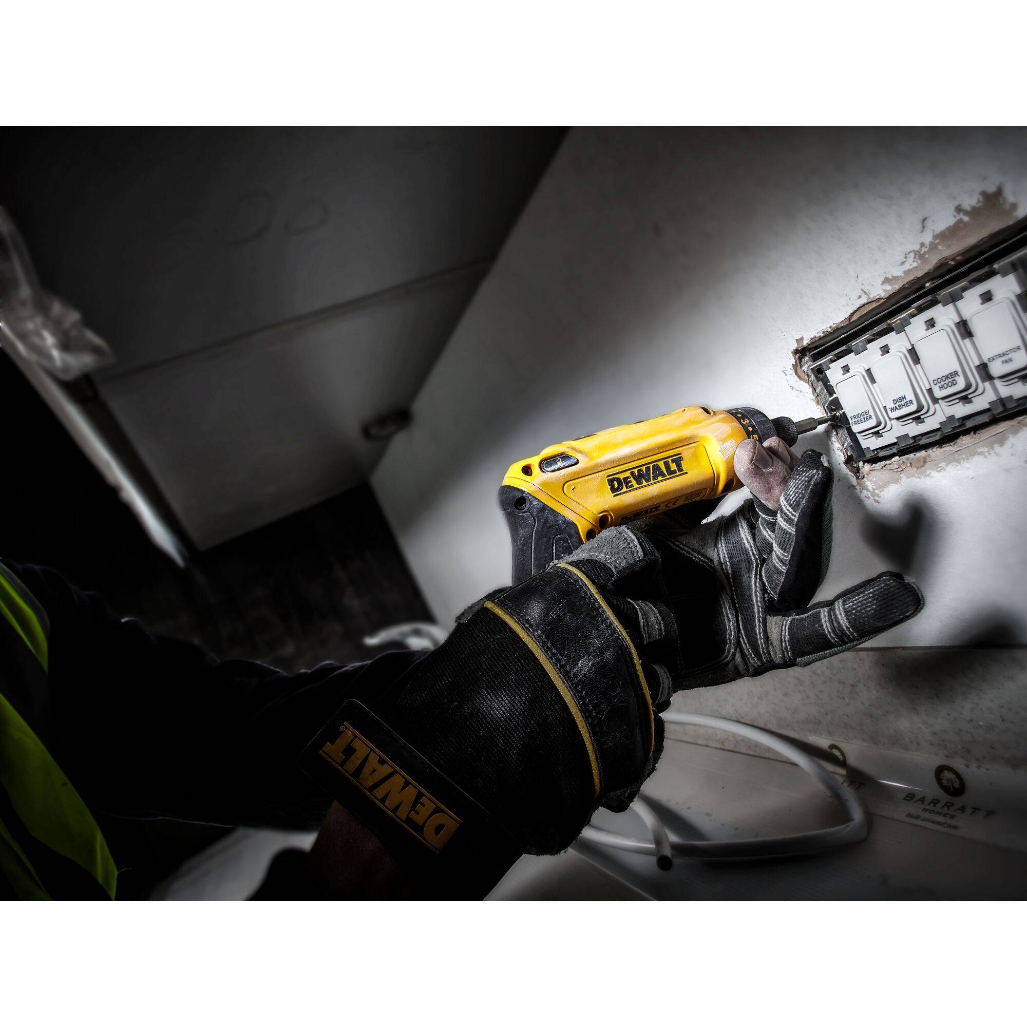 A person wearing black gloves is using a yellow power tool to work on a rectangular hole in the wall.