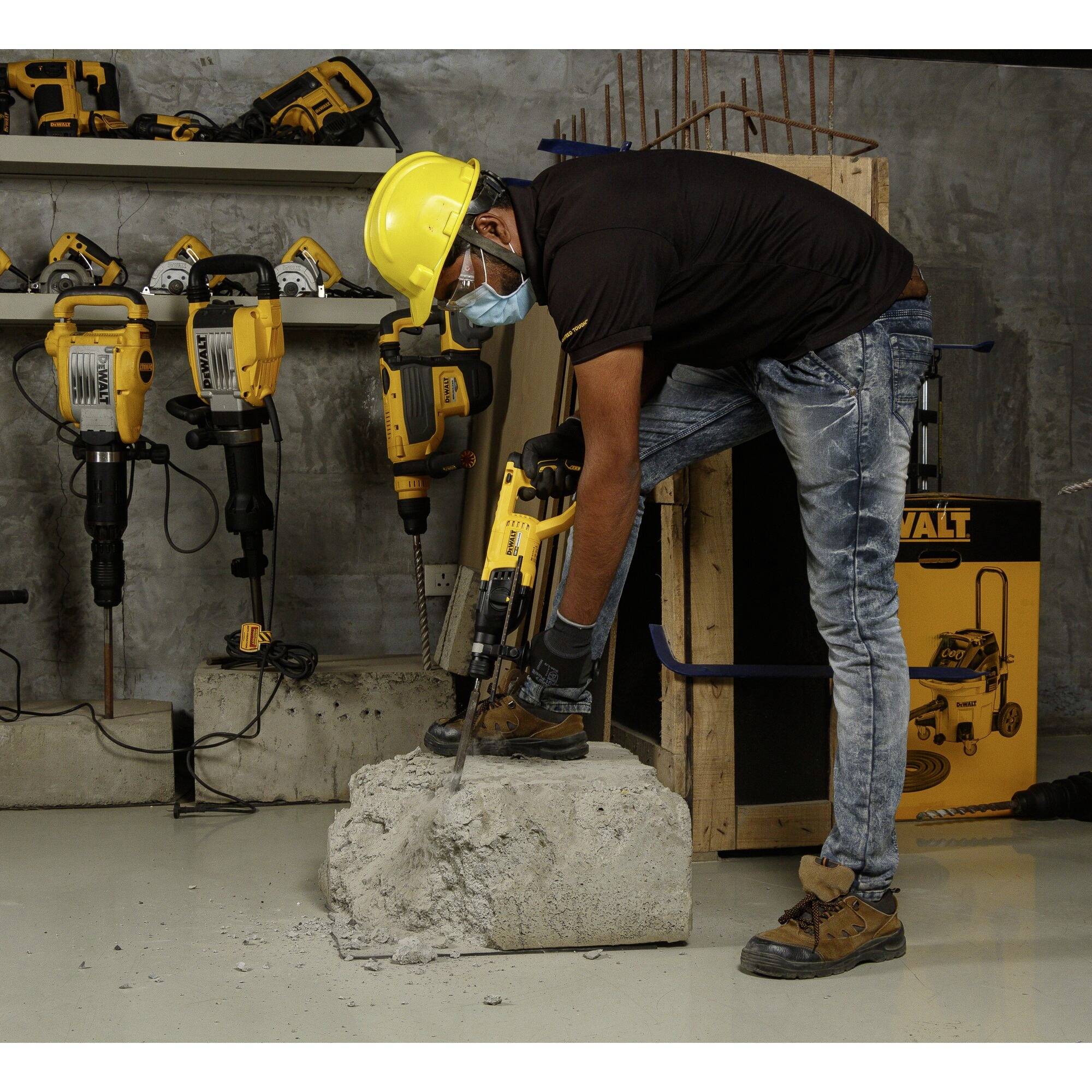 A man wearing a helmet and mask is drilling into a concrete block with an electric tool. Additional drilling equipment can be seen in the background.