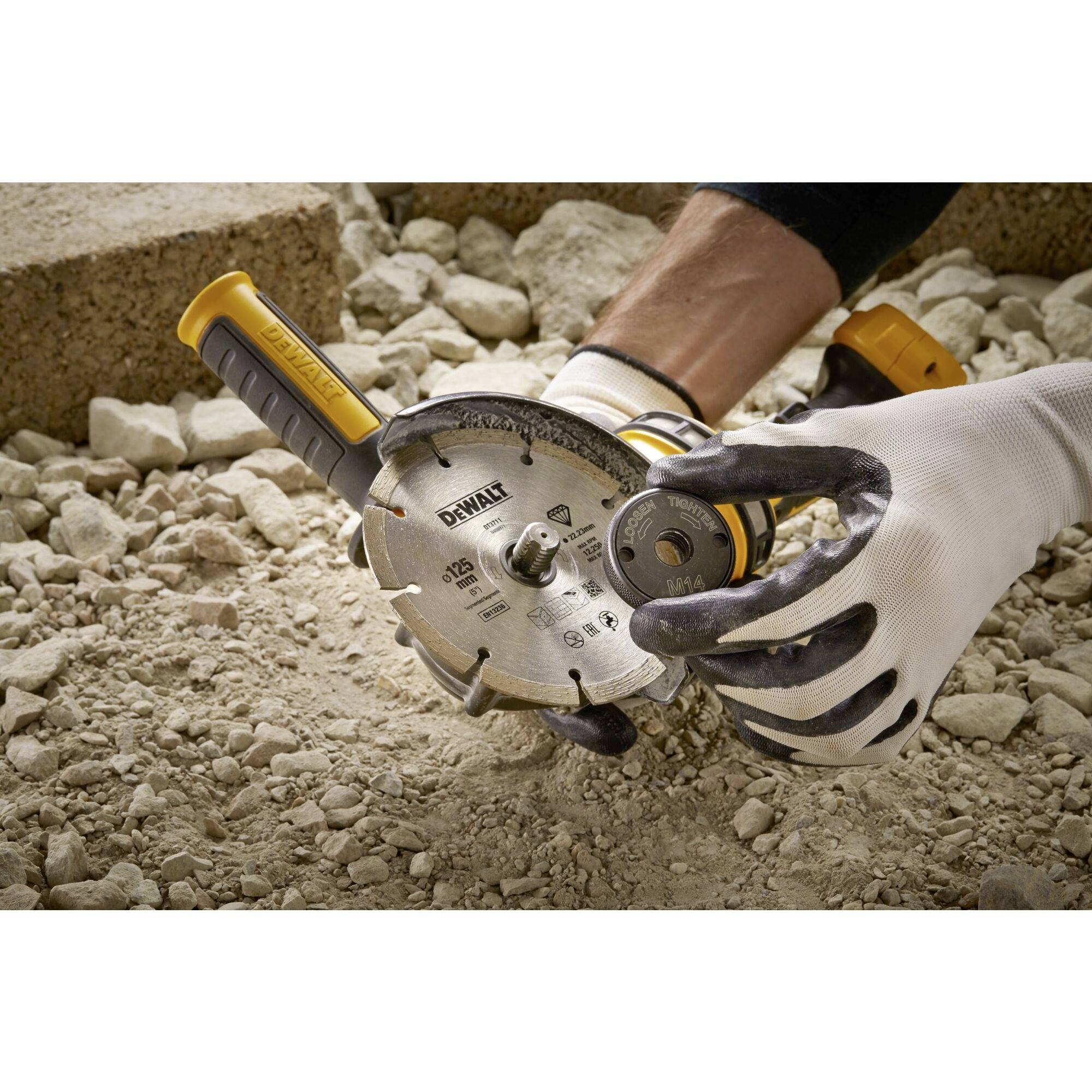 A person is wearing gloves and holding an electric cutting tool over a stony surface, ready for use.