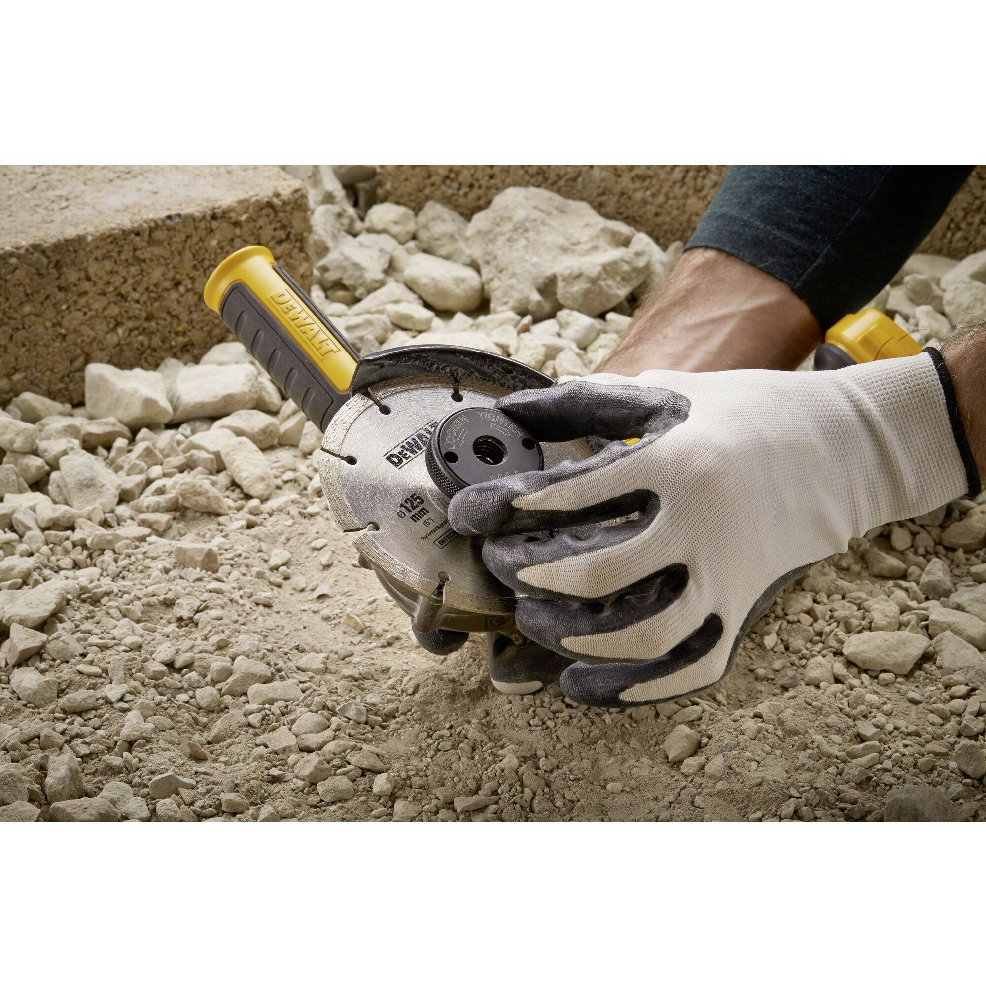 A person is holding a grinding machine, surrounded by gravel. They are wearing gloves for safety while working.