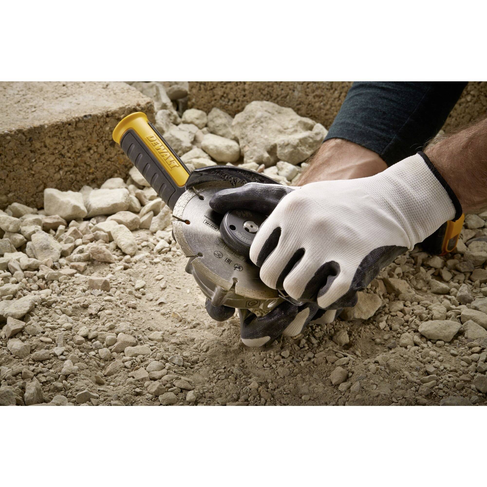 A person is wearing gloves and holding a grinding machine over a stony floor, ready to process the material.