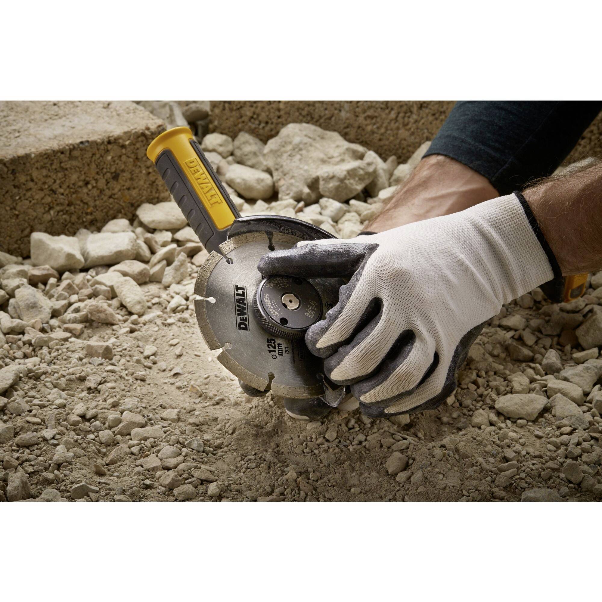 A tradesman wearing protective gloves is holding an electric cutting disc, surrounded by gravel and sand, ready to cut.