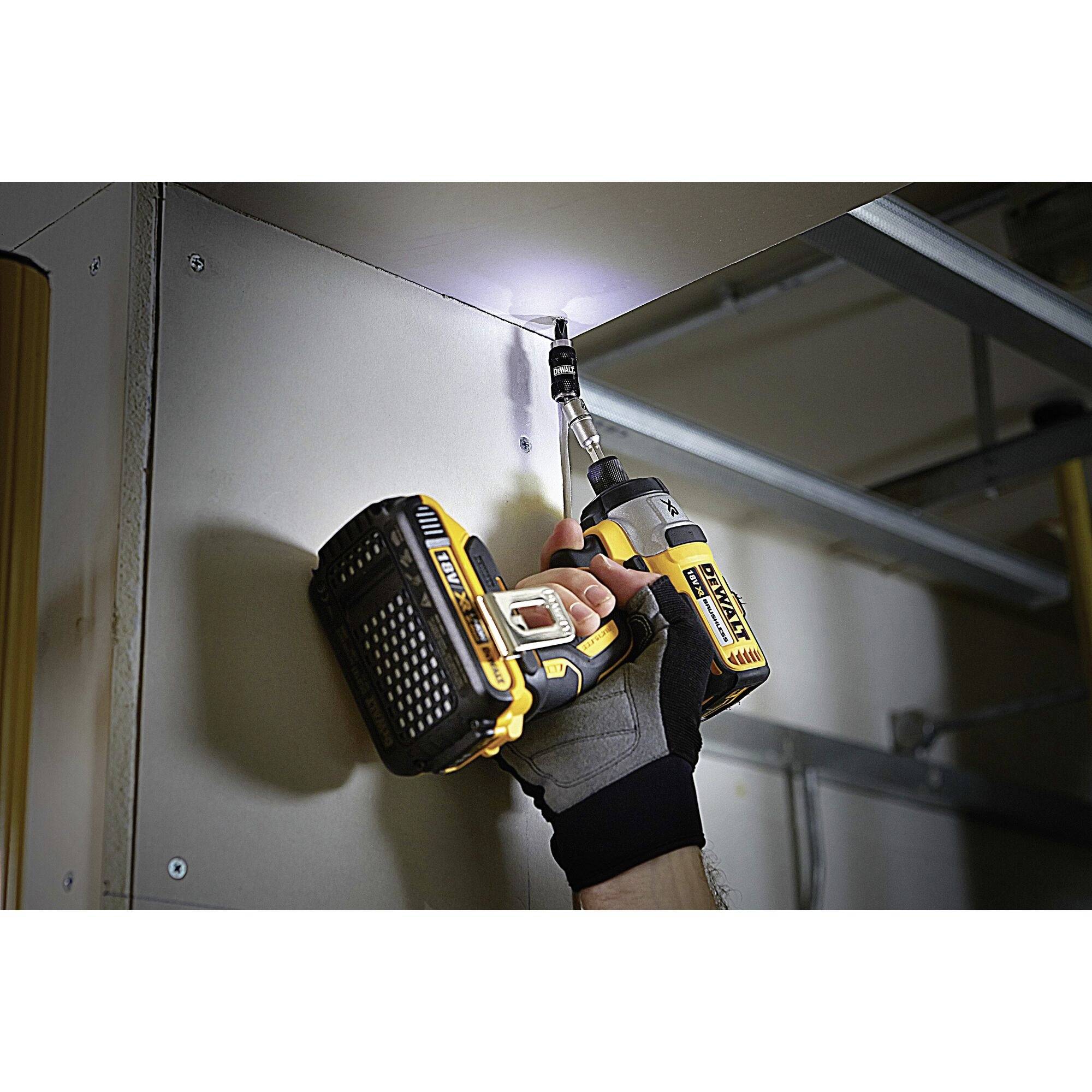 A person is holding a drill and screwing a screw into the ceiling. The drill is yellow and black, and the room is well-lit.