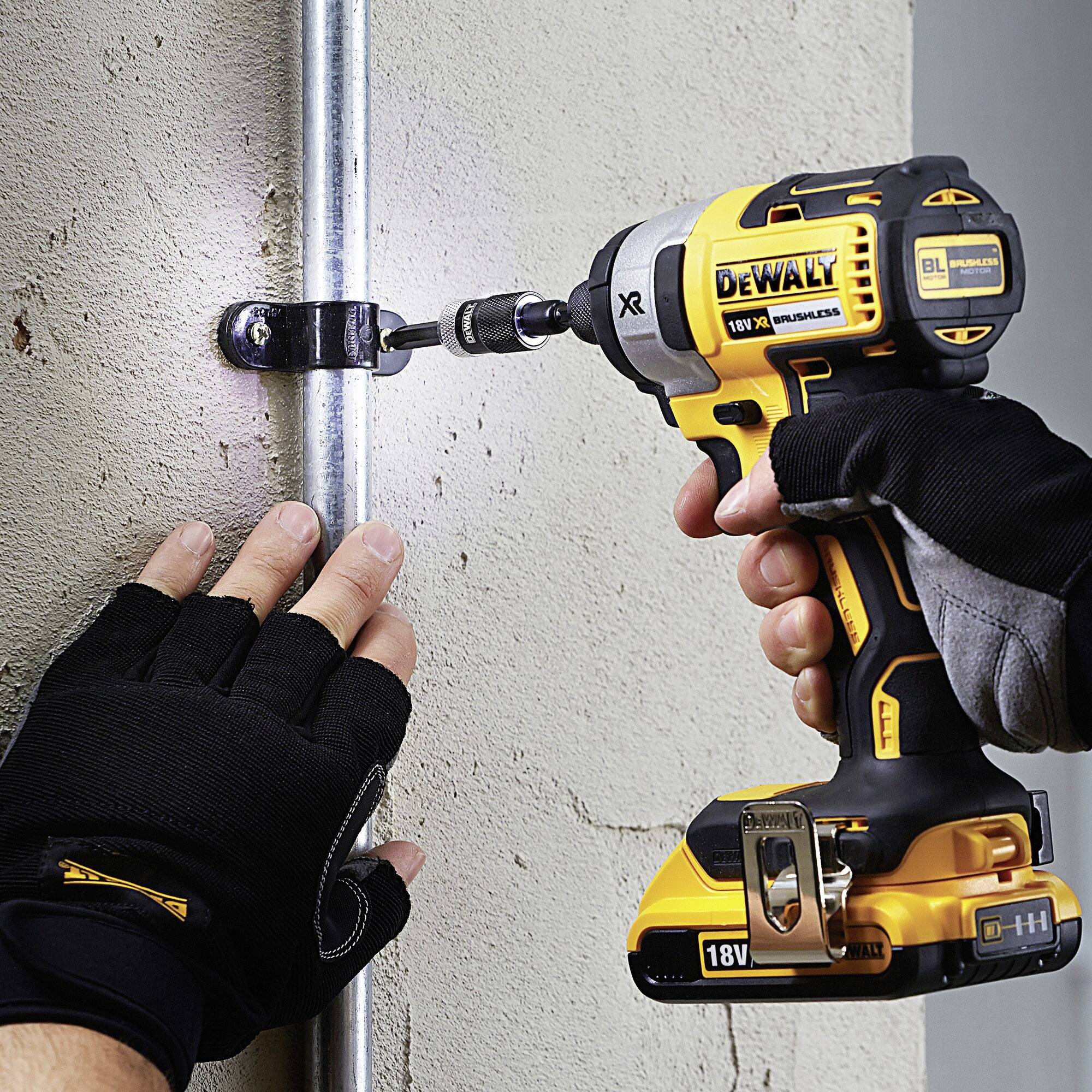 A person is holding a cordless drill and securing a metal rod to the wall with a screw. Gloves are protecting their hands.