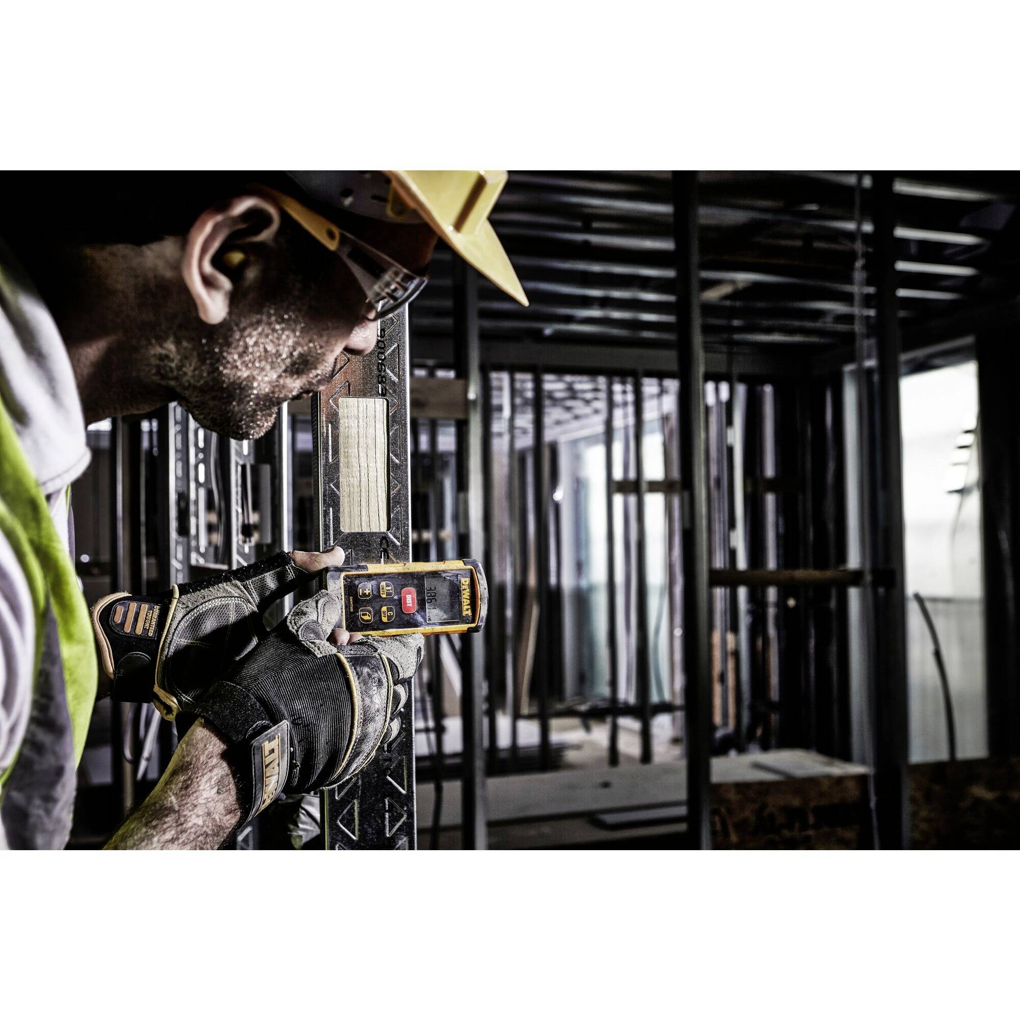 A worker wearing safety glasses and gloves is using a device to measure a metal structure on a construction site.