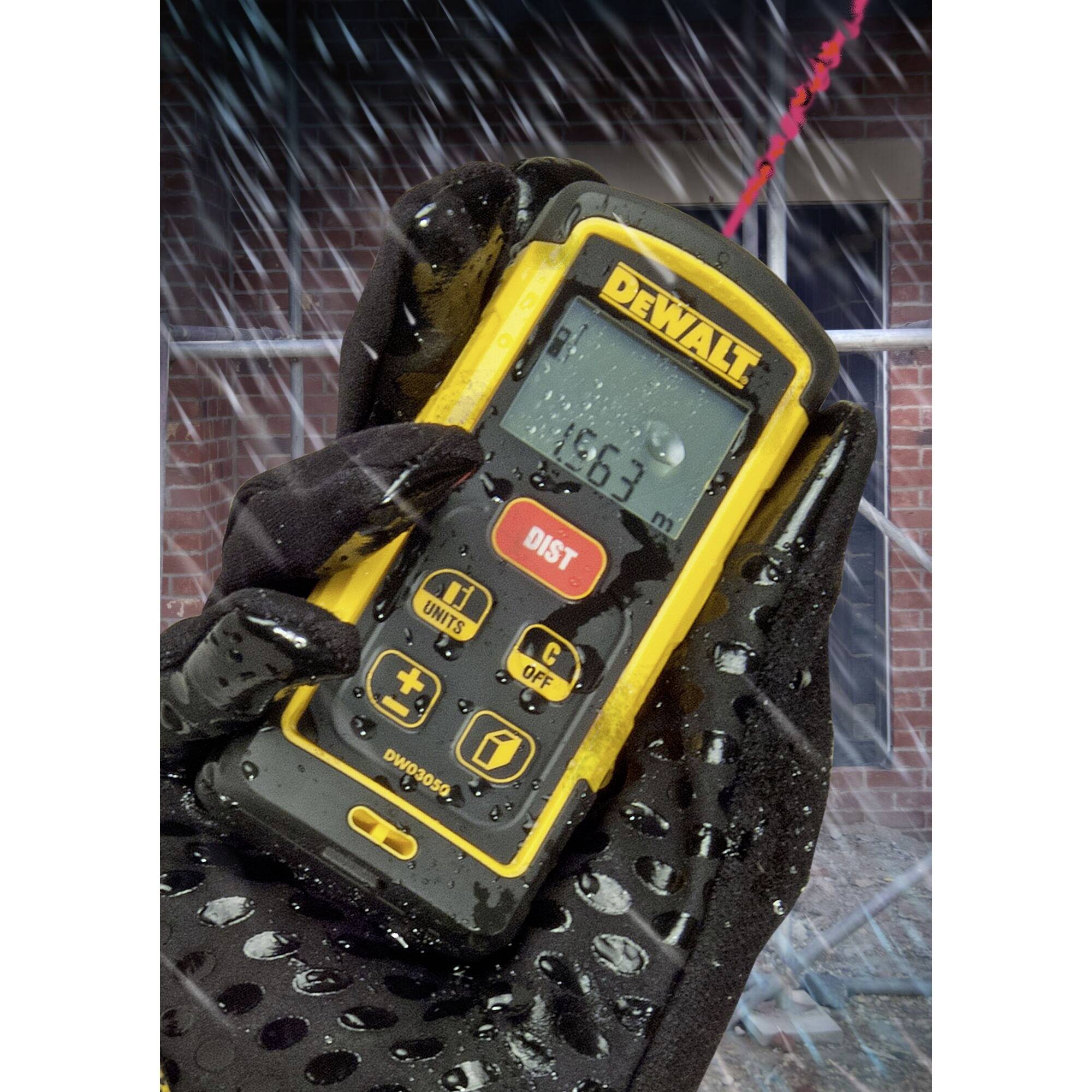 A gloved hand holds a yellow DeWalt distance measuring device in the rain. The screen displays '16.31 m'. Background blurred.