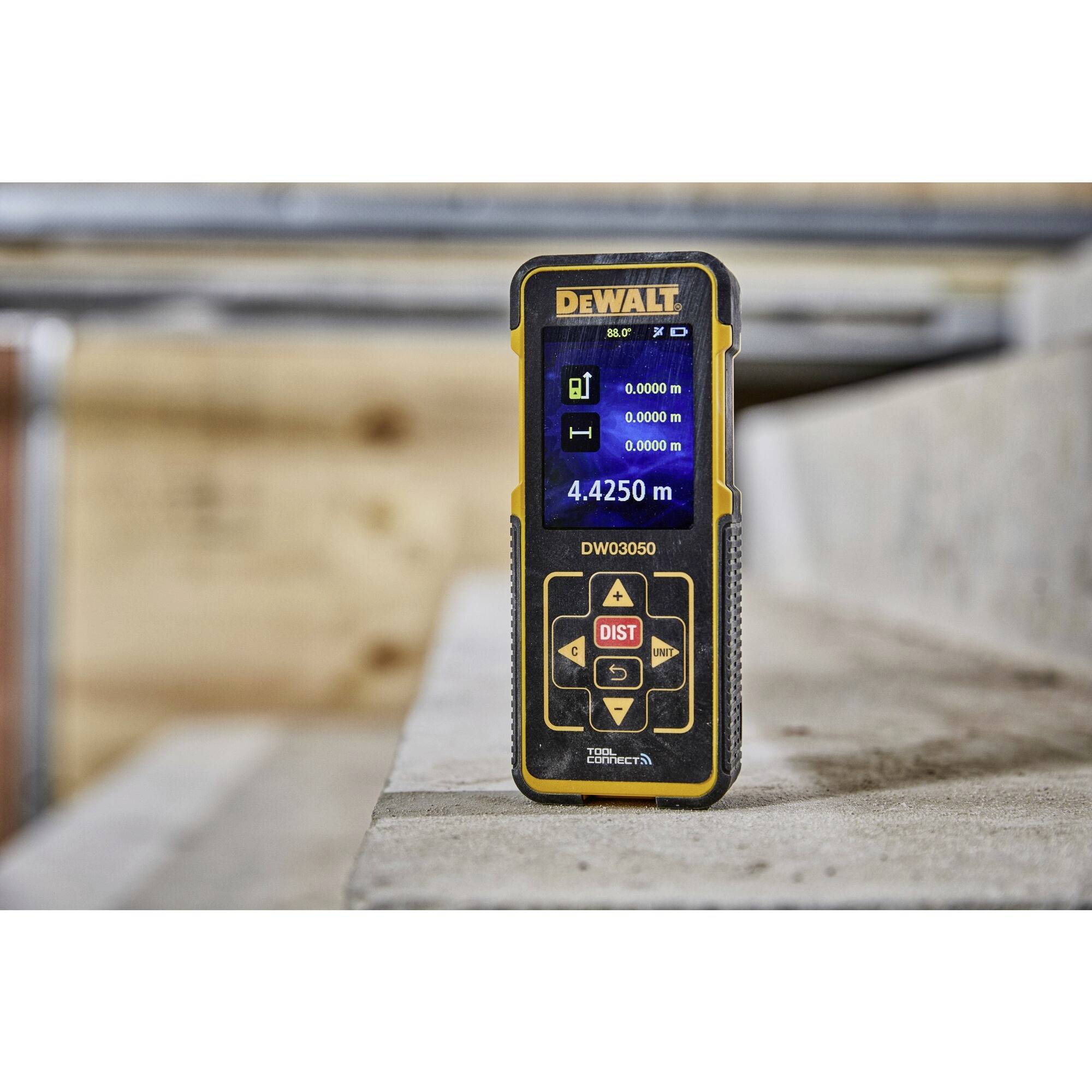 A DeWalt laser measuring device displays '4.4250 m' on a screen. It is resting on a concrete step in a construction environment.