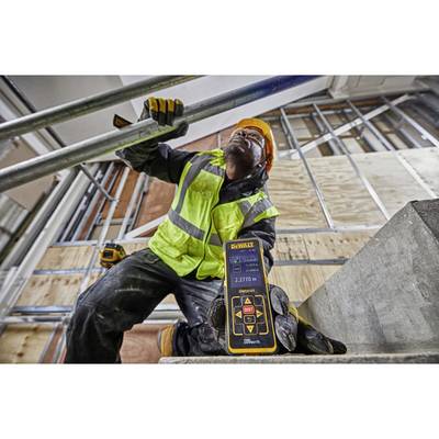 A construction worker in safety clothing is measuring the distance with a digital measuring device in an unfinished building.