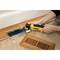 A person is using a yellow power tool to saw a rectangular hole in a wooden floor; a ventilation grille lies nearby.
