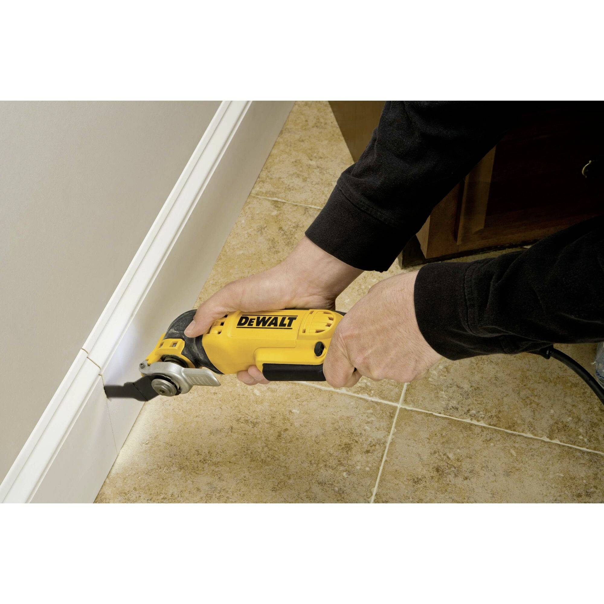 A person is using a yellow power tool to cut a strip on the wall on a tiled floor.