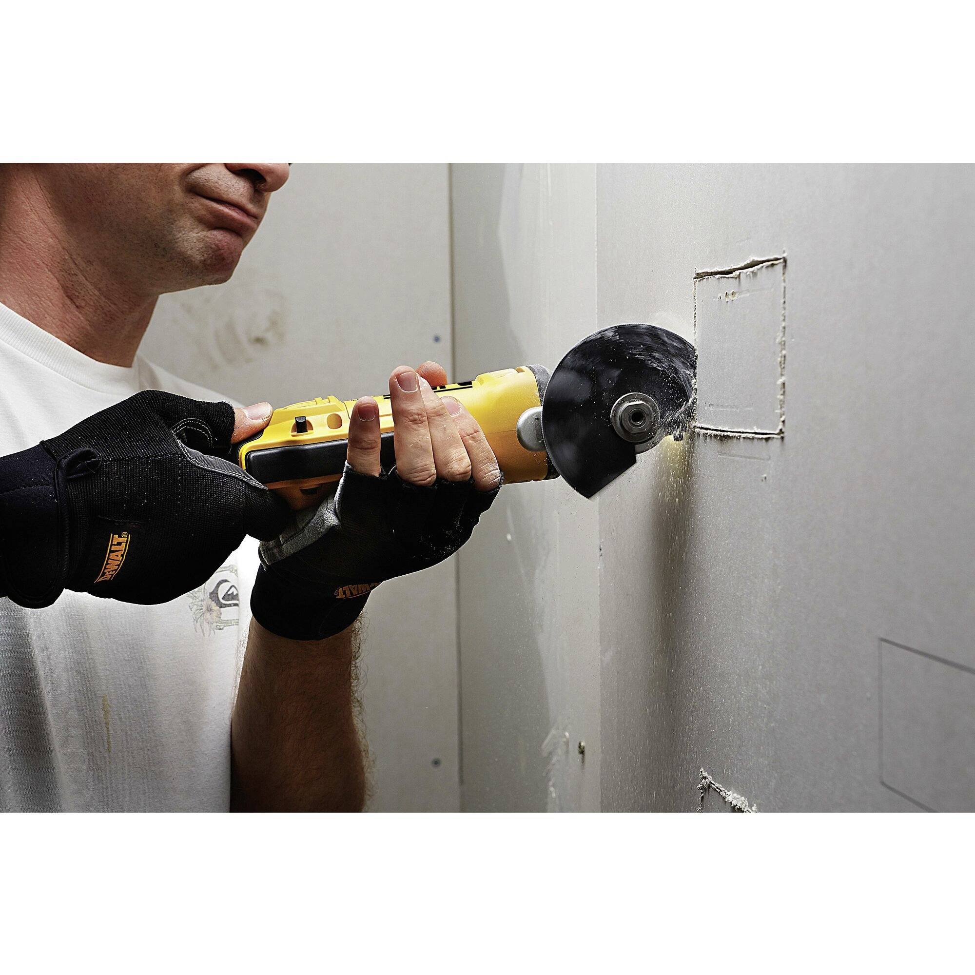 A man is cutting holes in a plasterboard wall using a rotary tool. He is wearing work gloves.