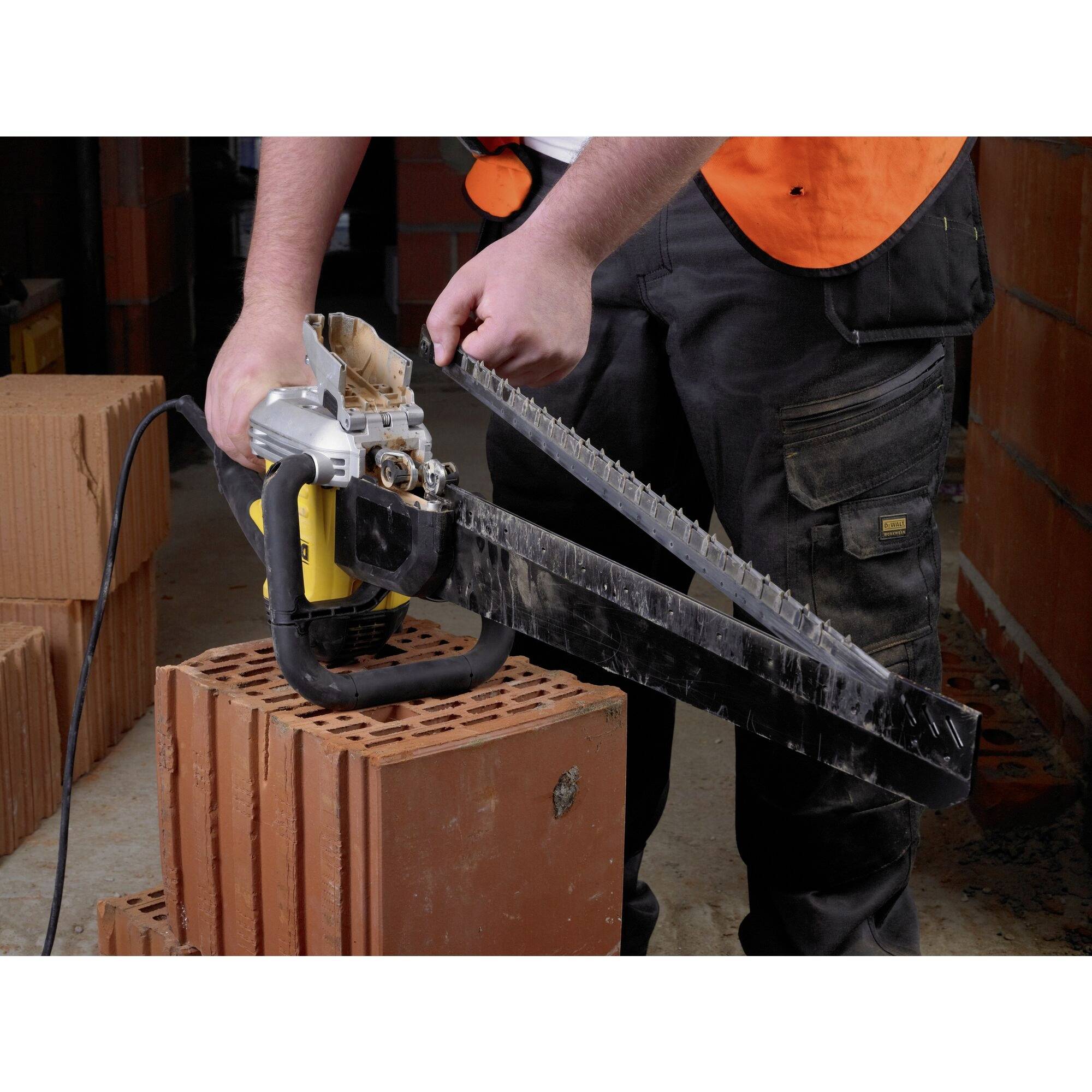 A man wearing a high-visibility orange safety vest is using an electric saw to cut bricks on a construction site.