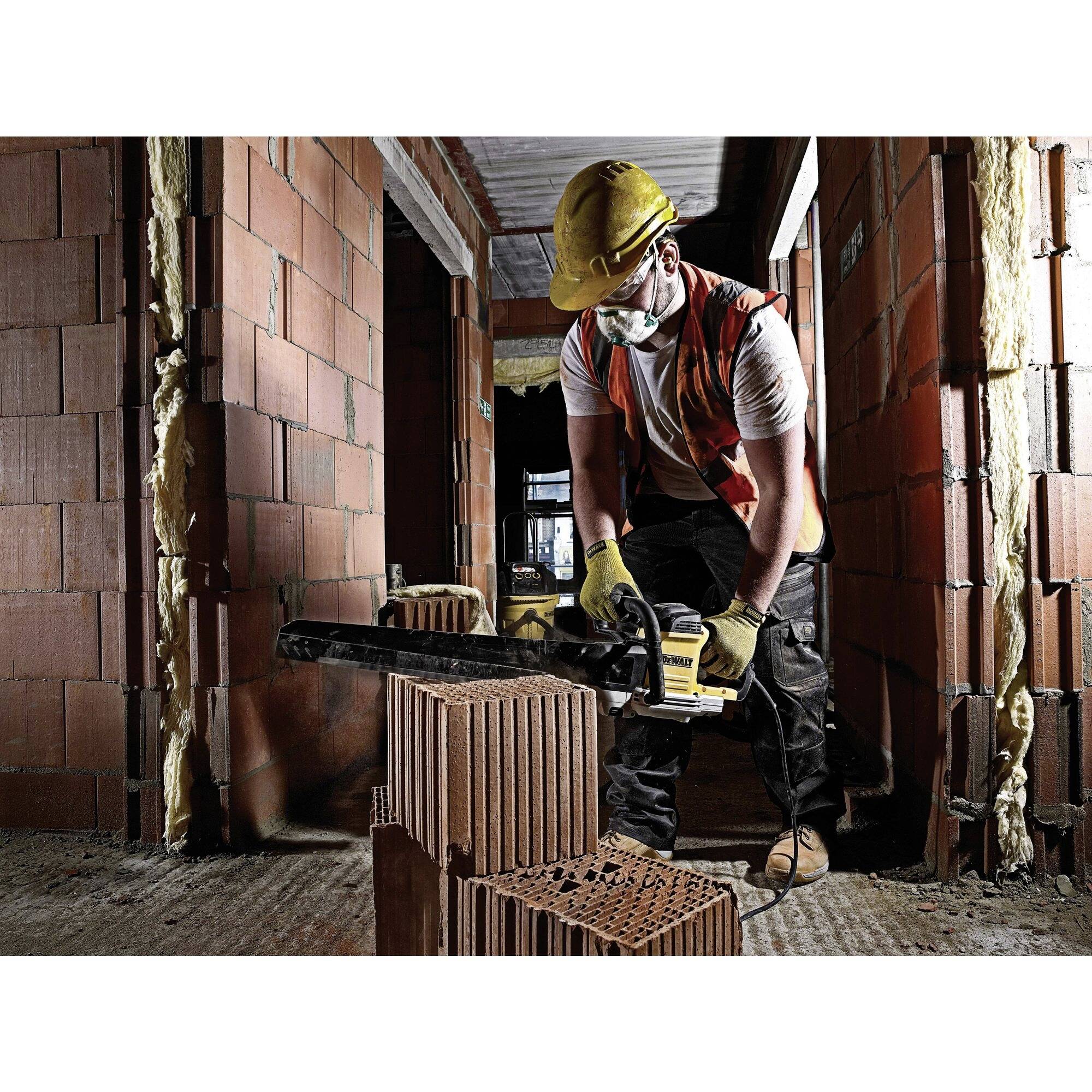 'Worker in protective clothing cutting a brick with a chainsaw in an unfinished building; construction site in a shell state.'