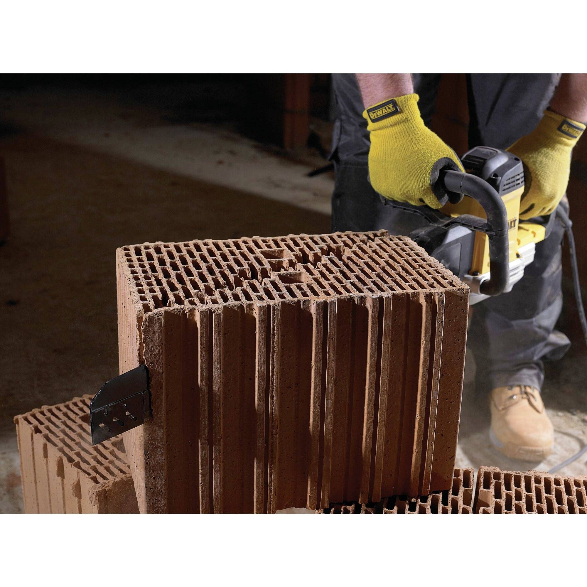 'A person wearing work gloves cuts through a porous brick with a chainsaw. Dust and fragments fly off.'