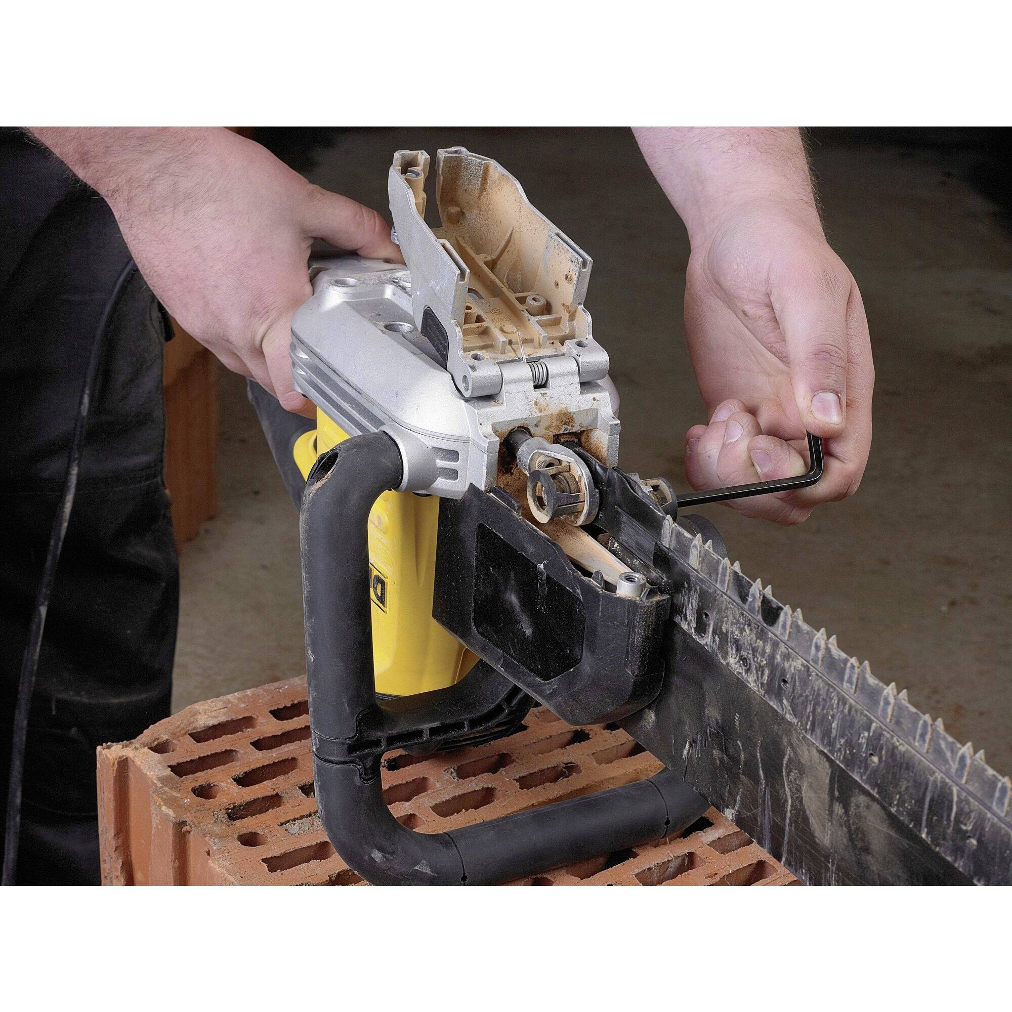 A person is adjusting the chain of a chainsaw on a brick block using an Allen key.
