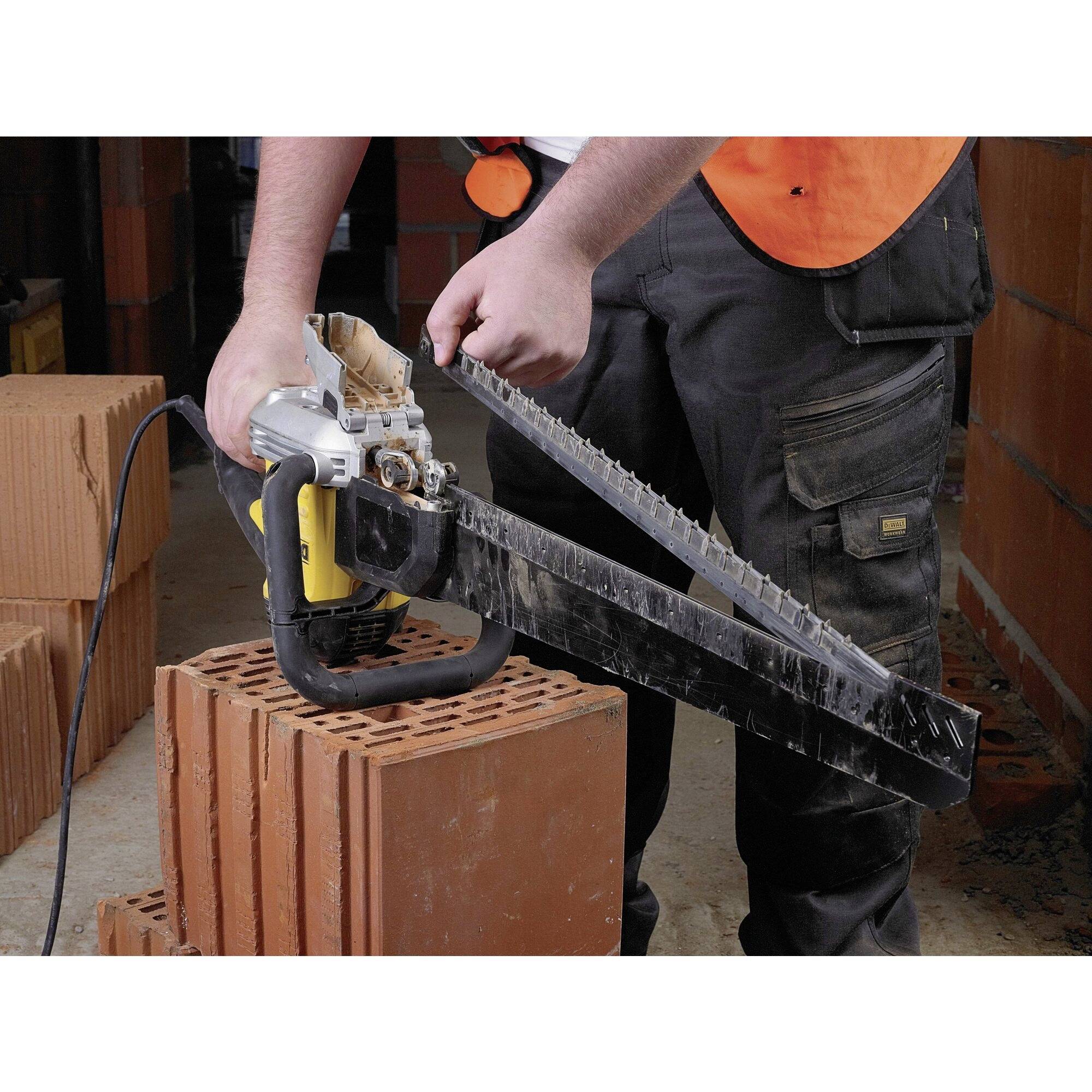 A person wearing work attire is cutting a brick with a chainsaw. Stacked bricks are visible in the background.