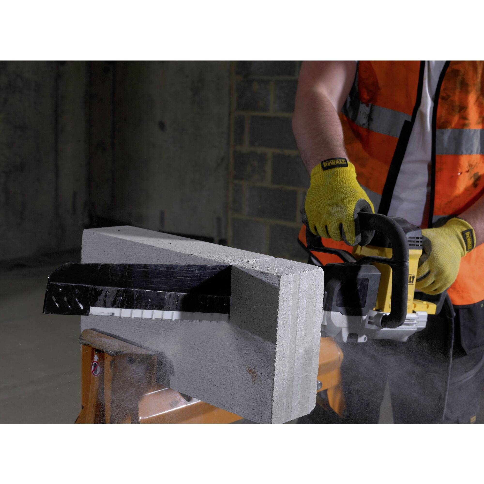 A person wearing safety clothing is cutting a large concrete block with an electric saw in a construction site environment.