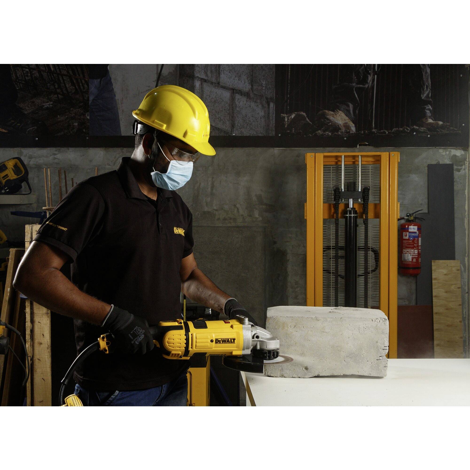 A person is wearing a safety helmet and mask and using an electric tool to grind a concrete block in a workshop environment.