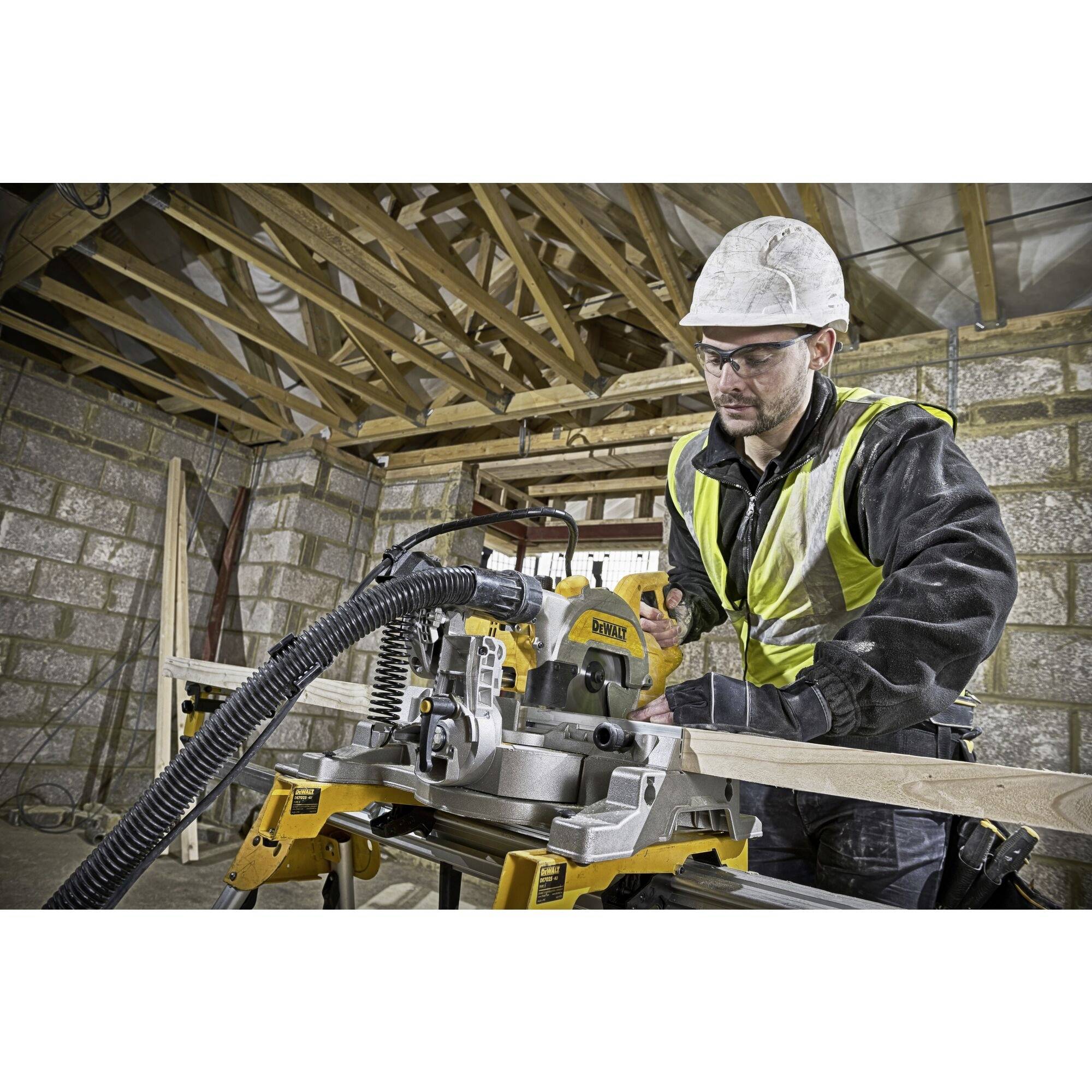 A construction worker wearing protective clothing and a hard hat is cutting wood with an electric saw in an unfinished wooden structure.