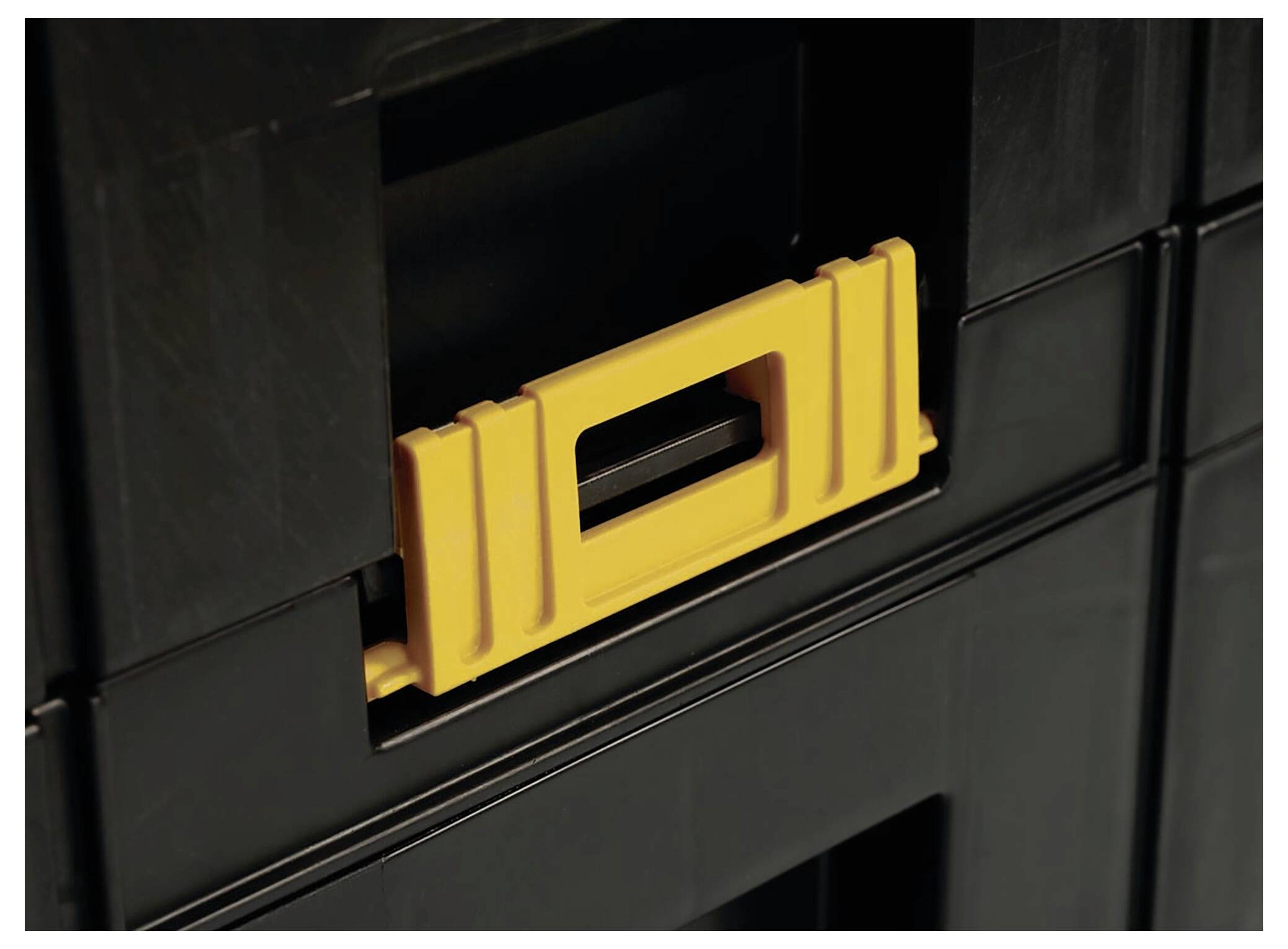 A yellow handle on a black, stackable plastic storage box.