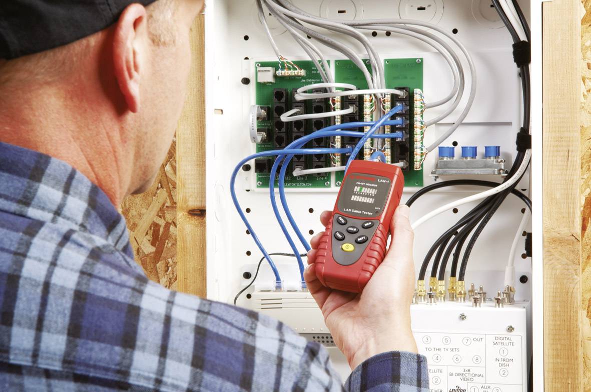 A technician is checking the wiring in a fuse box with a digital testing device.