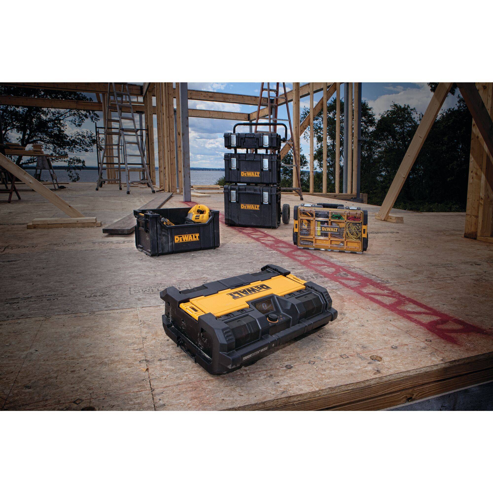 On a building site, several yellow and black toolboxes stand on a wooden floor. Unfinished wooden structures are visible in the background.