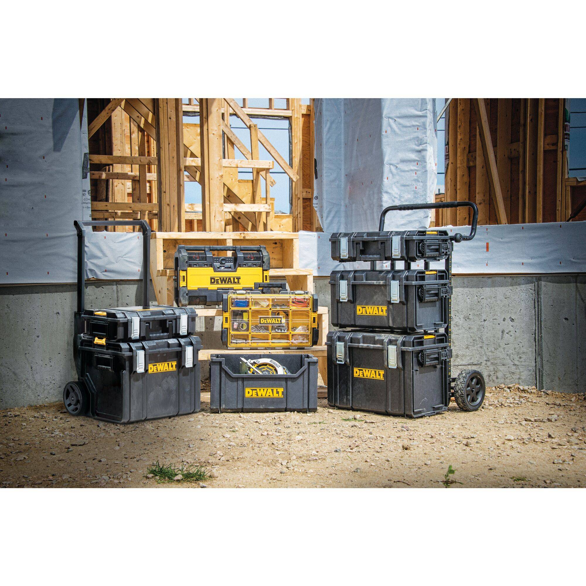 Toolboxes of various sizes and types on a construction site in front of a partially completed wooden building.