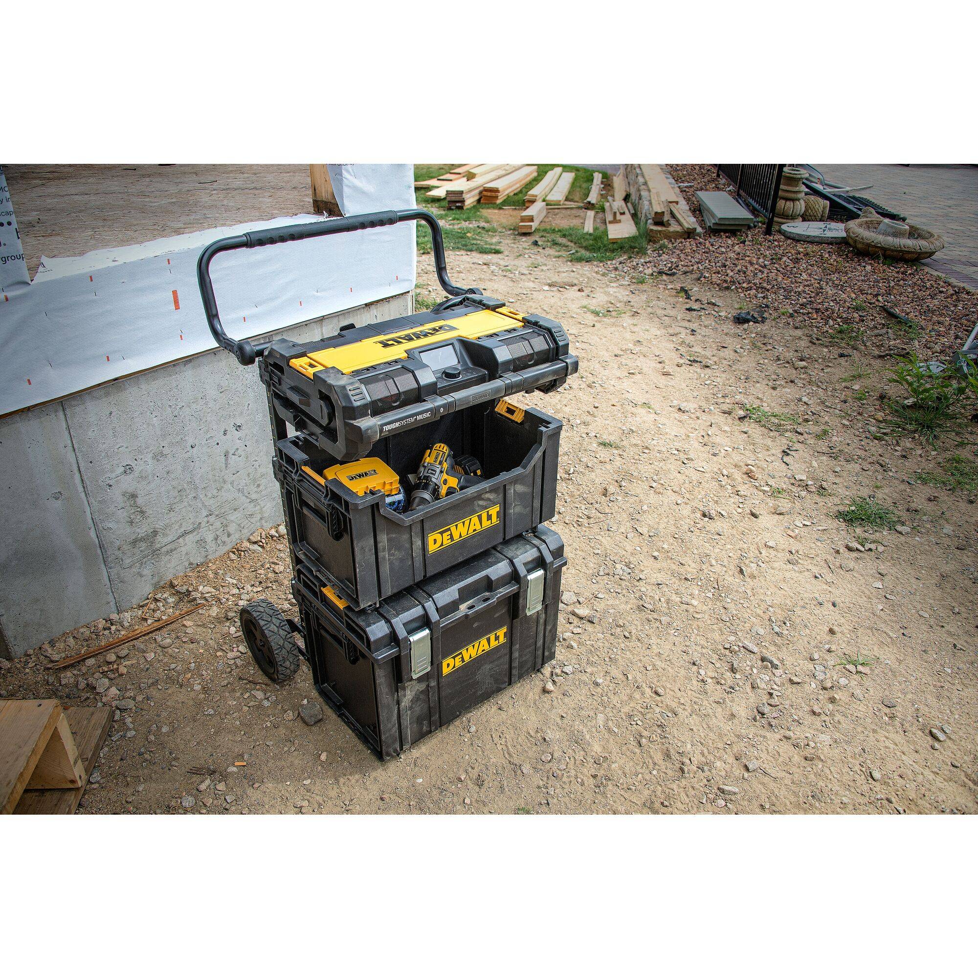A stack of yellow and black toolboxes with wheels stands on a building site next to a building.