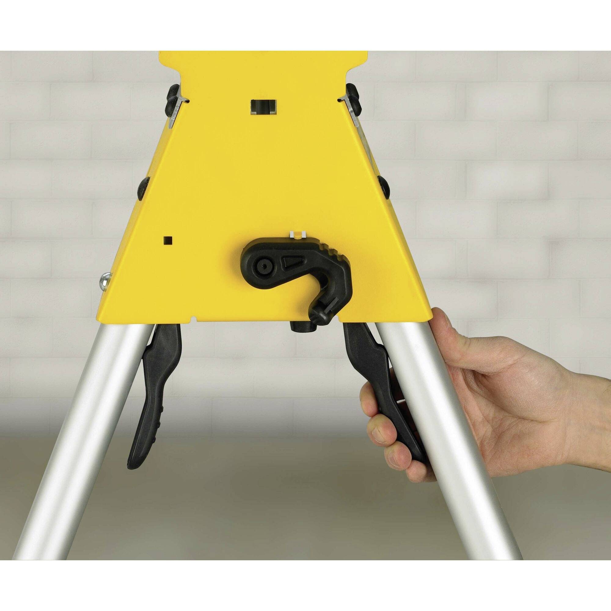 A hand adjusts a yellow, three-legged tripod with a black lever mechanism, background out of focus.