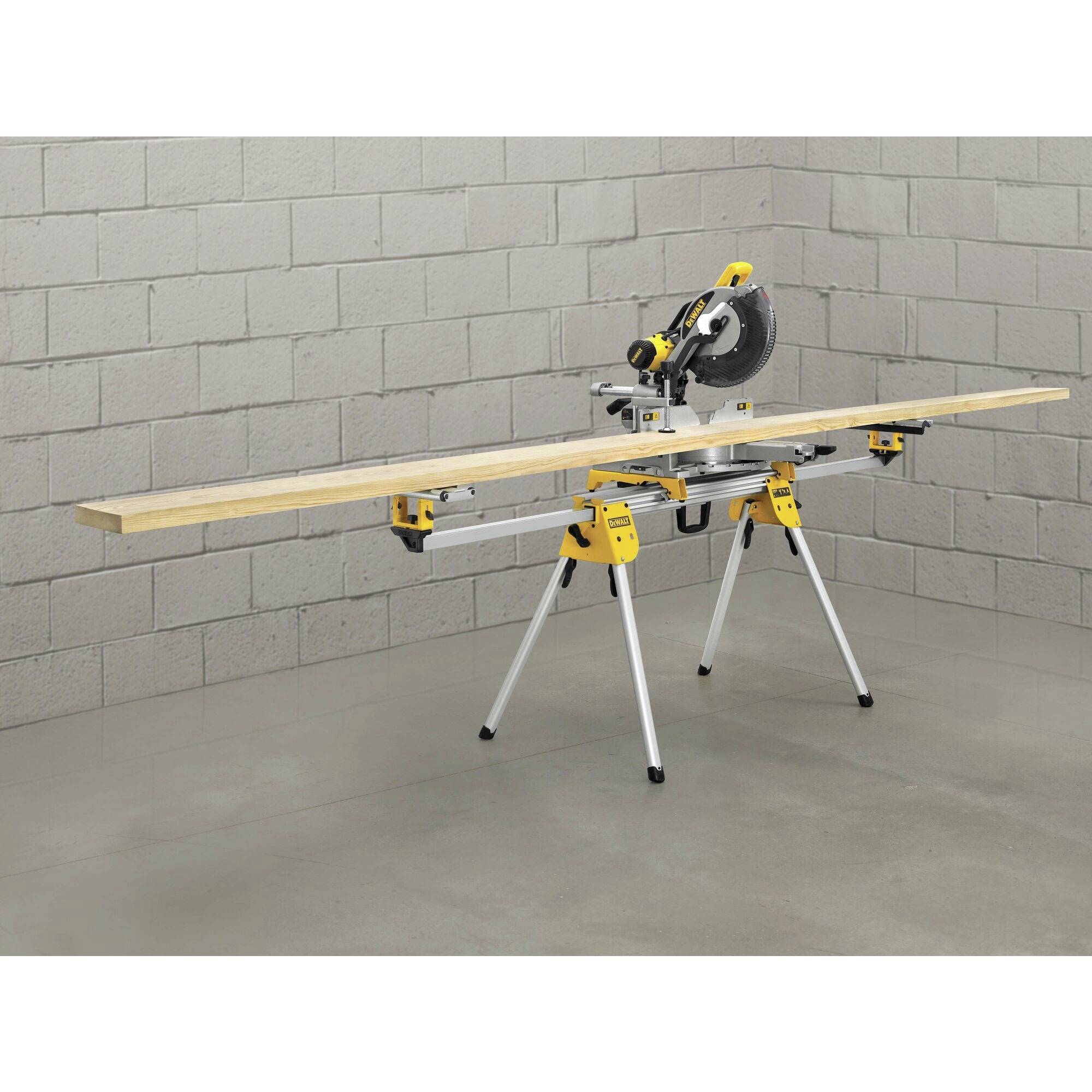 An electric mitre saw mounted on a sturdy stand with a large wooden board prepared for cutting, in a workshop.