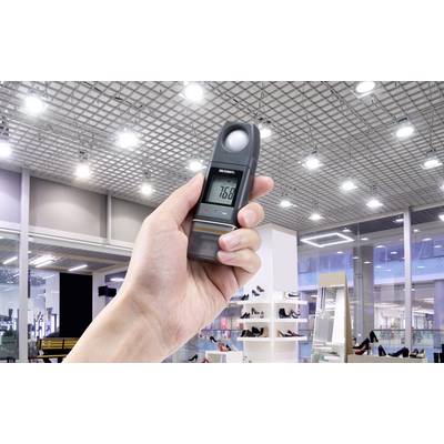 Someone is holding a light meter in a well-lit sales room. The device is displaying the value '766' on its digital display.