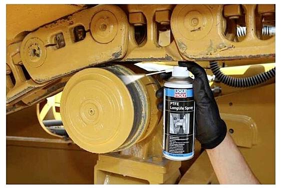 A person wearing a black glove sprays 'Liqui Moly PTFE Longlife Spray' on a metal part of a machinery, suggesting maintenance work.