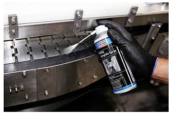 'Gloved hand sprays lubricant on a metal conveyor belt, showing maintenance work on industrial equipment.'