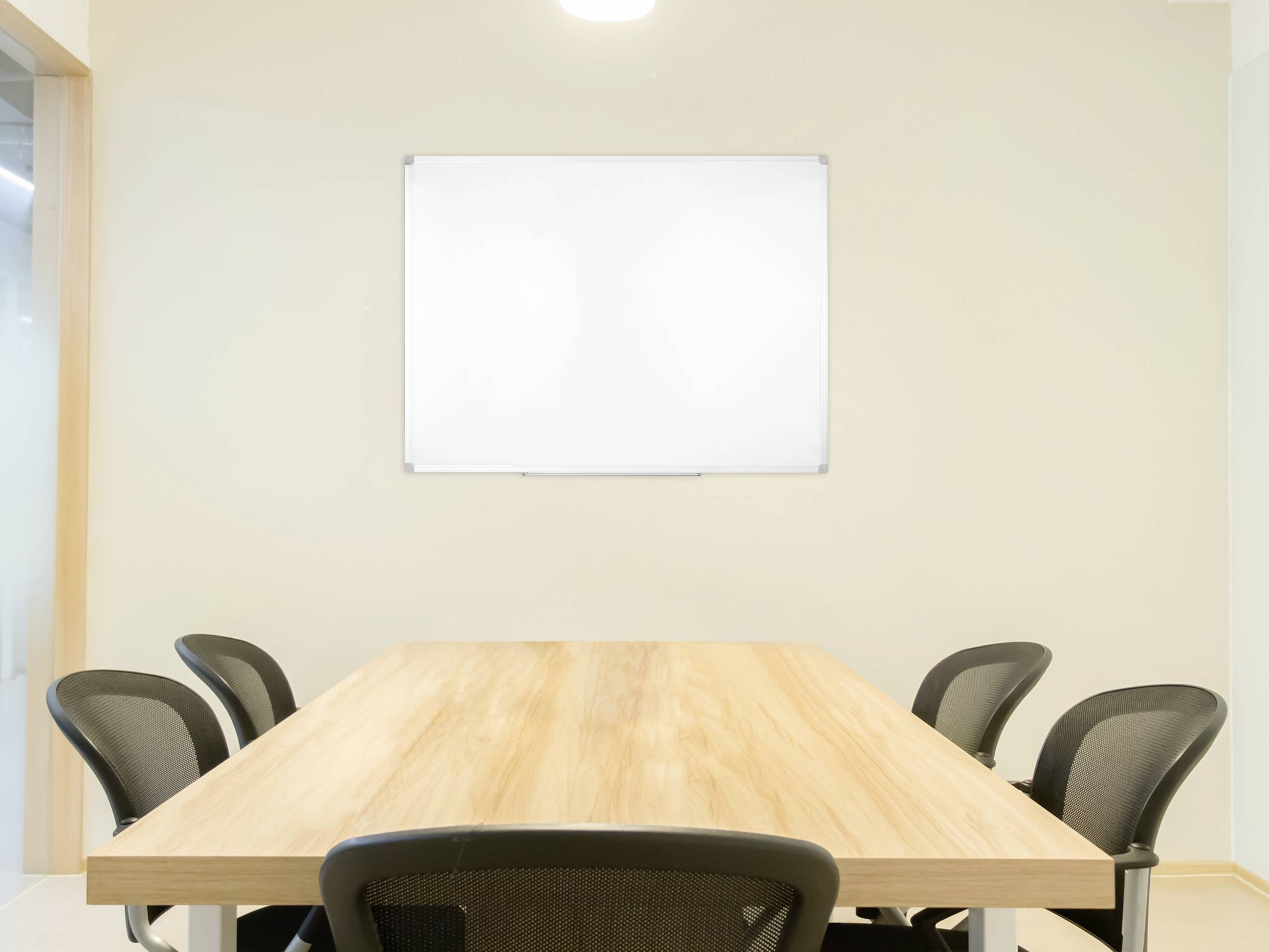 A meeting room with a wooden table, surrounded by six black office chairs. An empty white whiteboard hangs on the wall.