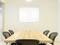 A meeting room with a wooden table, surrounded by six black office chairs. An empty white whiteboard hangs on the wall.