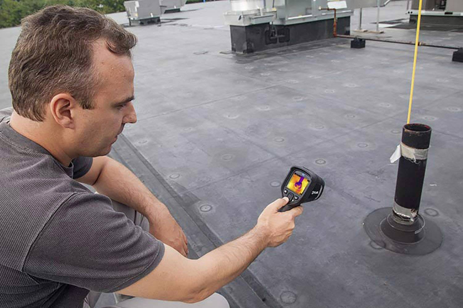 A man is using a thermal imaging camera to measure the temperature on a flat roof. The camera displays different colour ranges.