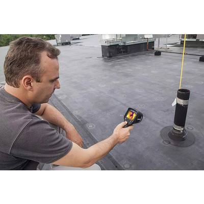 A man is using a thermal imaging camera to measure the temperature on a flat roof. The camera displays different colour ranges.