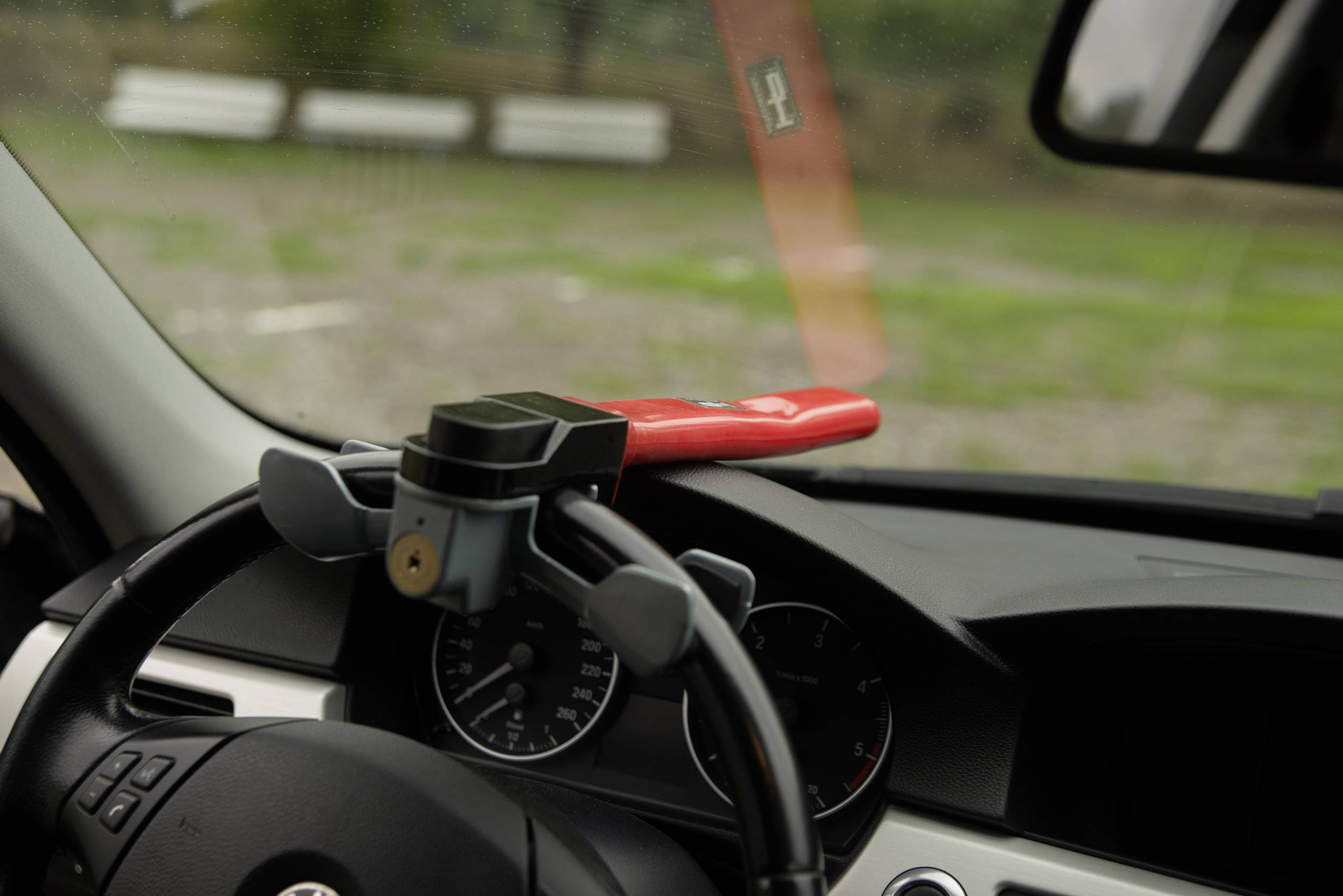 A red steering wheel lock is installed inside a car. It is attached to the steering wheel to prevent theft.