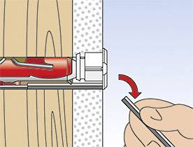 A hand pulls a red wall plug from a wooden wall using pliers; the wall plug is being extracted to the right, with an arrow indicating the direction.