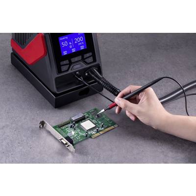 A person is soldering with a soldering iron on a circuit board, held by a hand. A soldering station displays temperature readings on a screen.