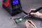 A person is soldering a green circuit board, holding a soldering iron and tweezers. The soldering iron station shows temperature: 50°C, air: 200.