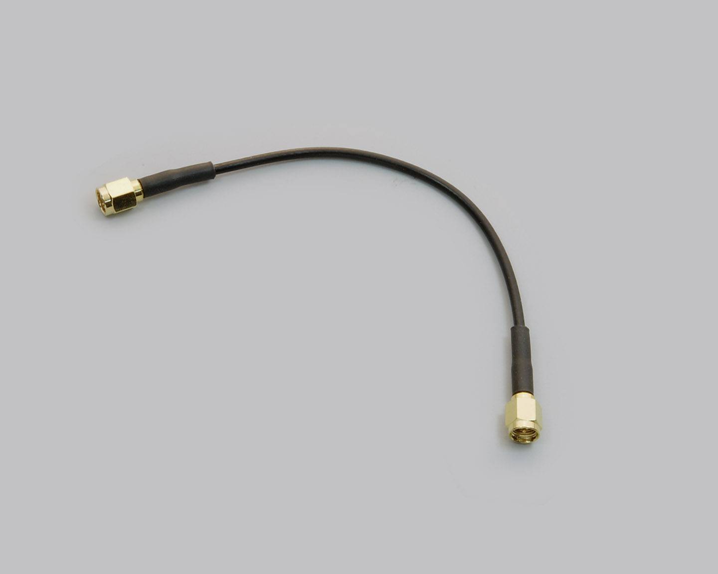 A short black coaxial cable with golden connectors at both ends lies on a grey background.