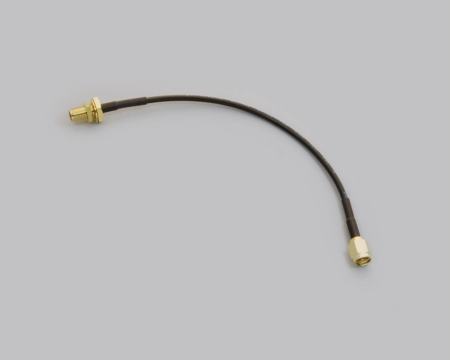 A black coaxial cable with gold-plated connectors at both ends, lying on a grey background.