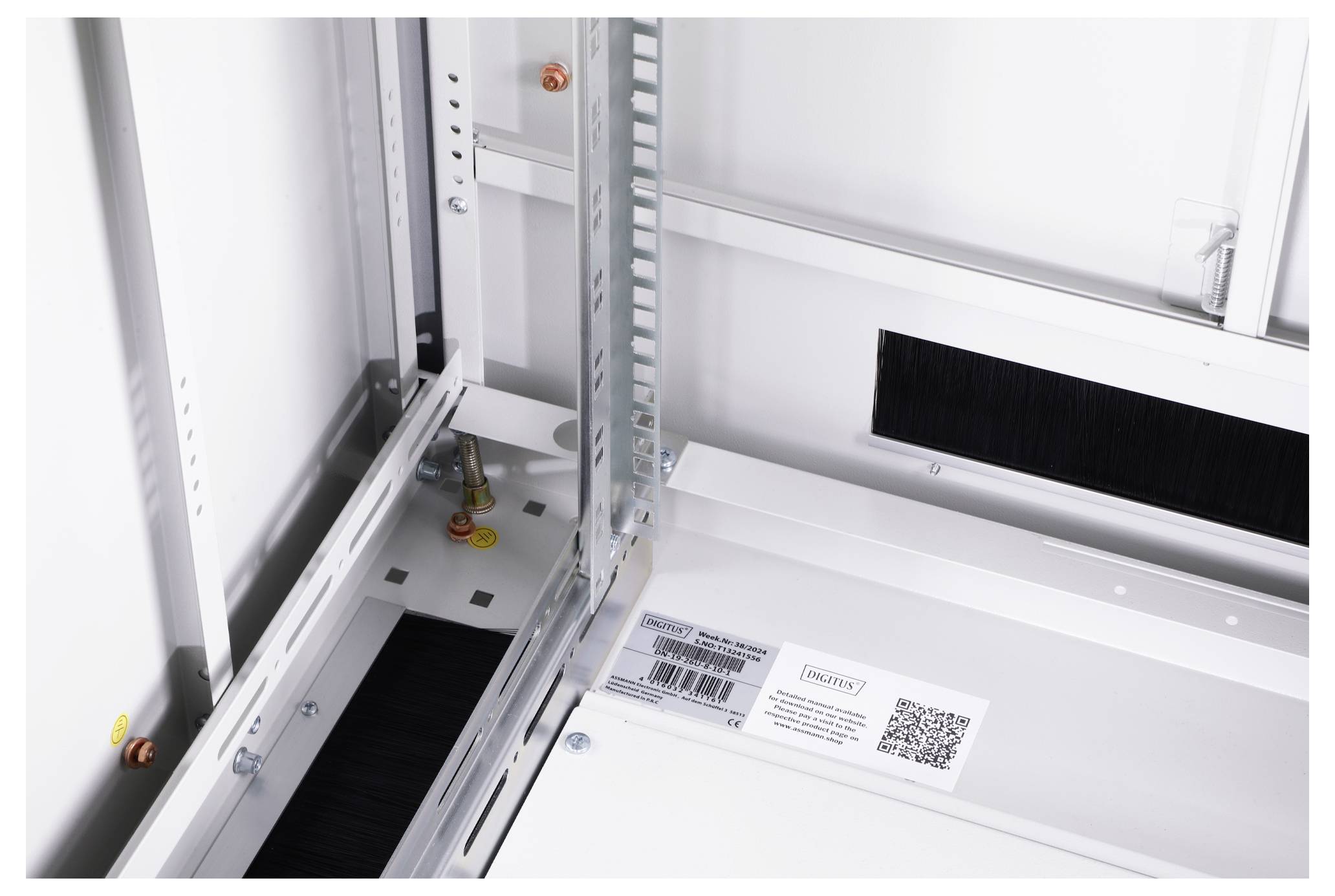 Interior view of a white equipment cabinet with a metal frame and a QR code on a surface. Cable openings and mounting elements visible.